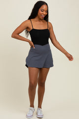 woman wearing a black sleeveless bodysuit with a gray wrap skirt and white sneakers