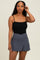 woman wearing a black tank top with gray swim skirt, standing against a neutral background