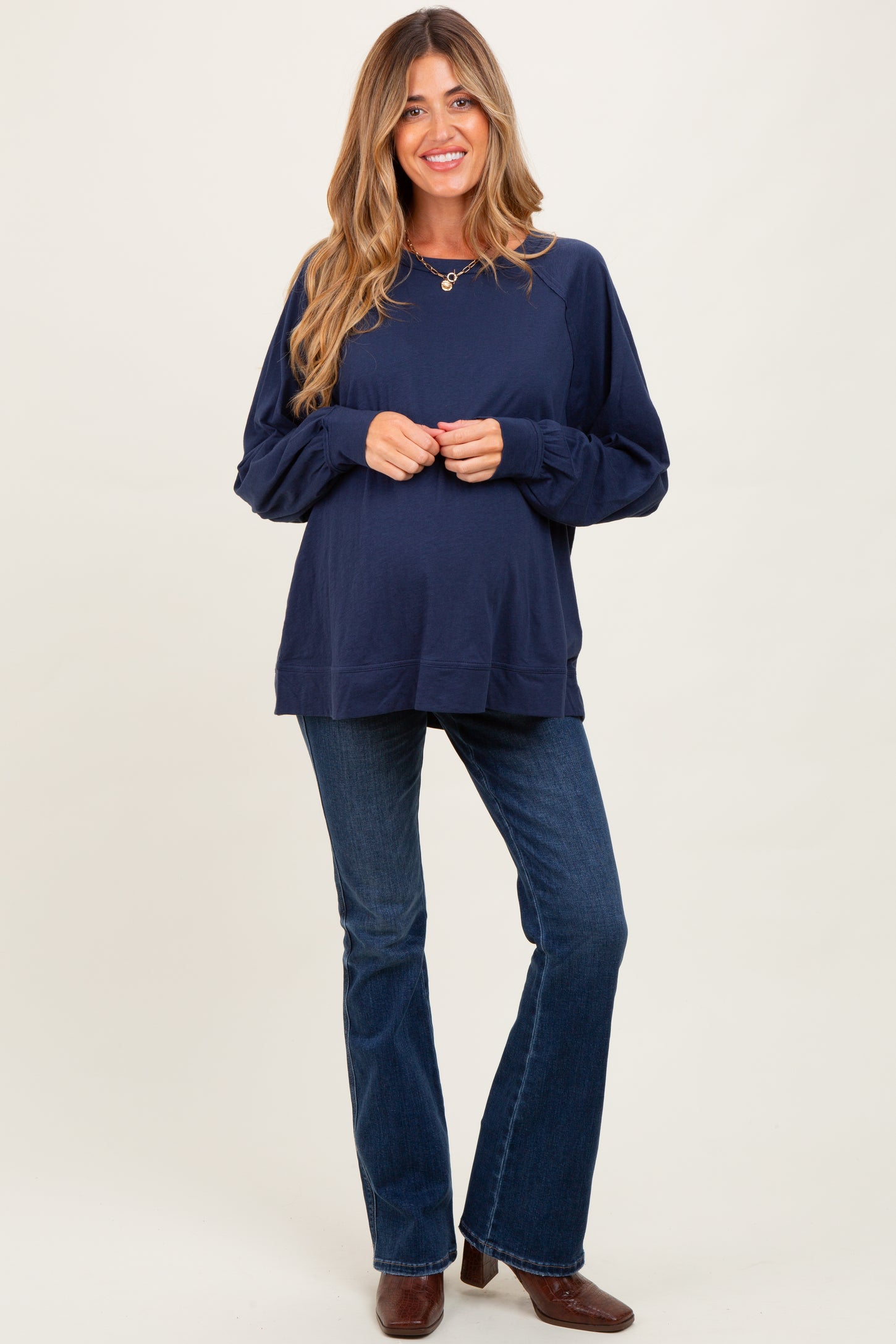 woman wearing a navy blue oversized maternity sweatshirt and flared jeans, holding her baby bump