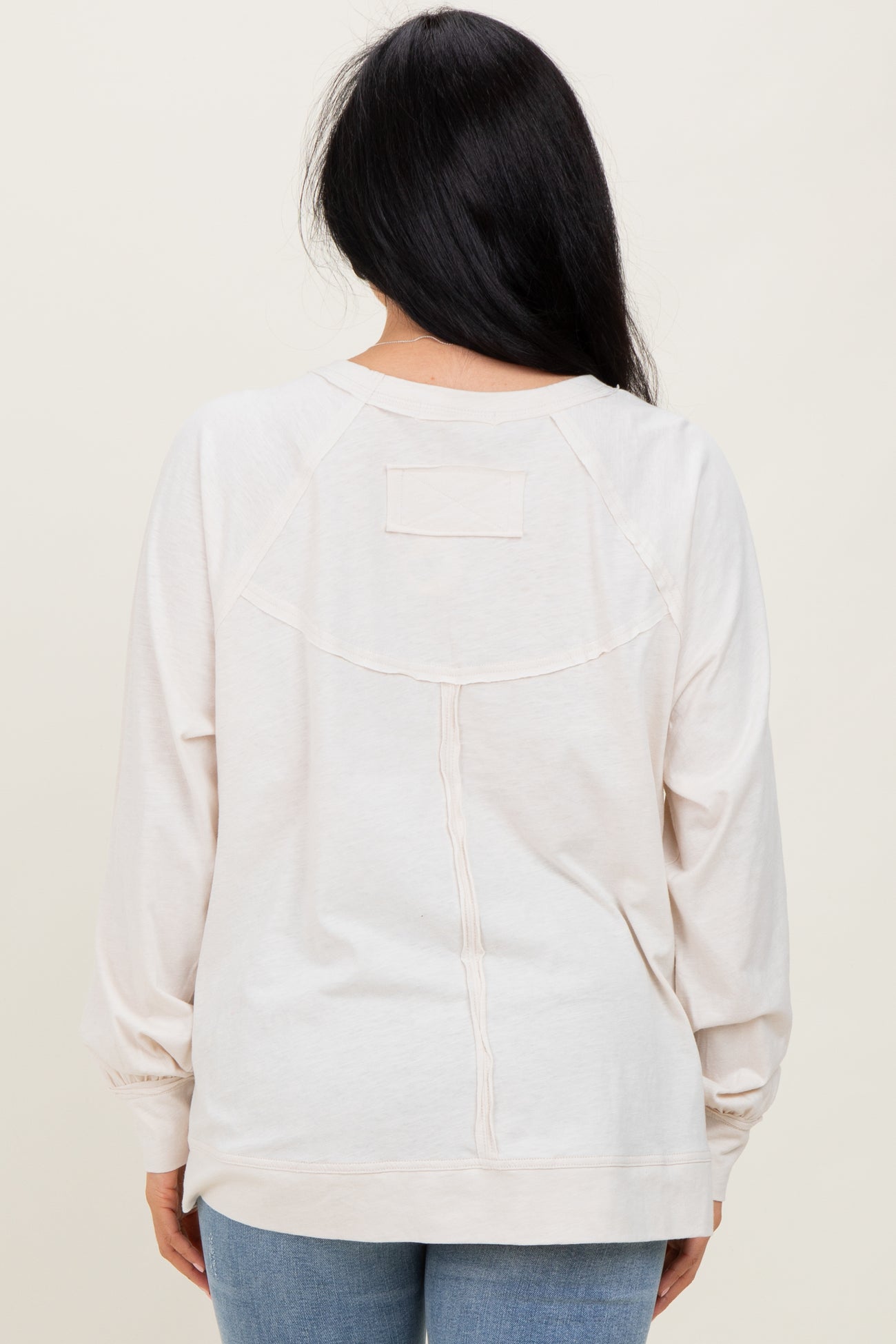 woman wearing a light beige long sleeve sweatshirt with a relaxed fit and back design detail