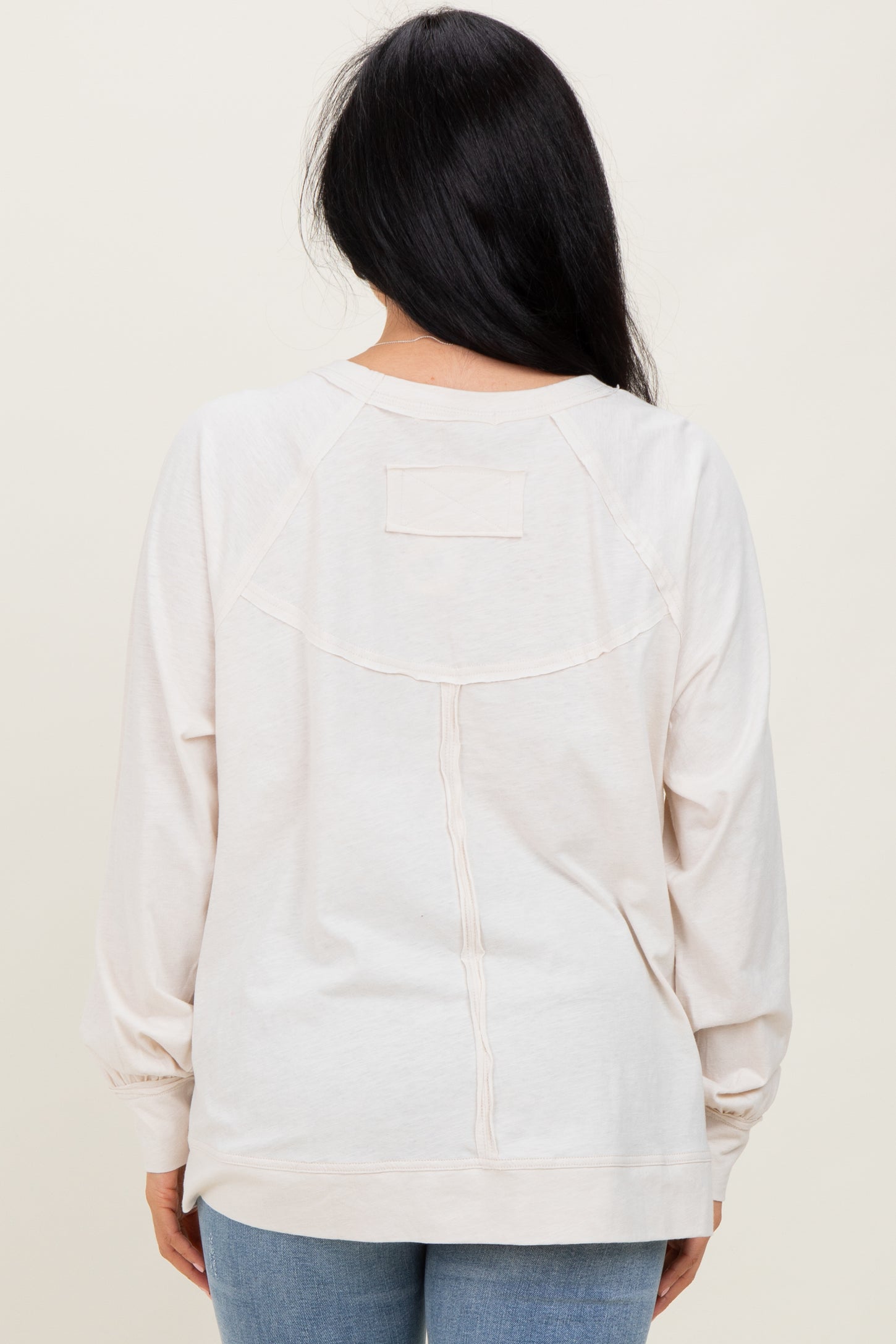 woman wearing a light beige long sleeve sweatshirt with a relaxed fit and back design detail