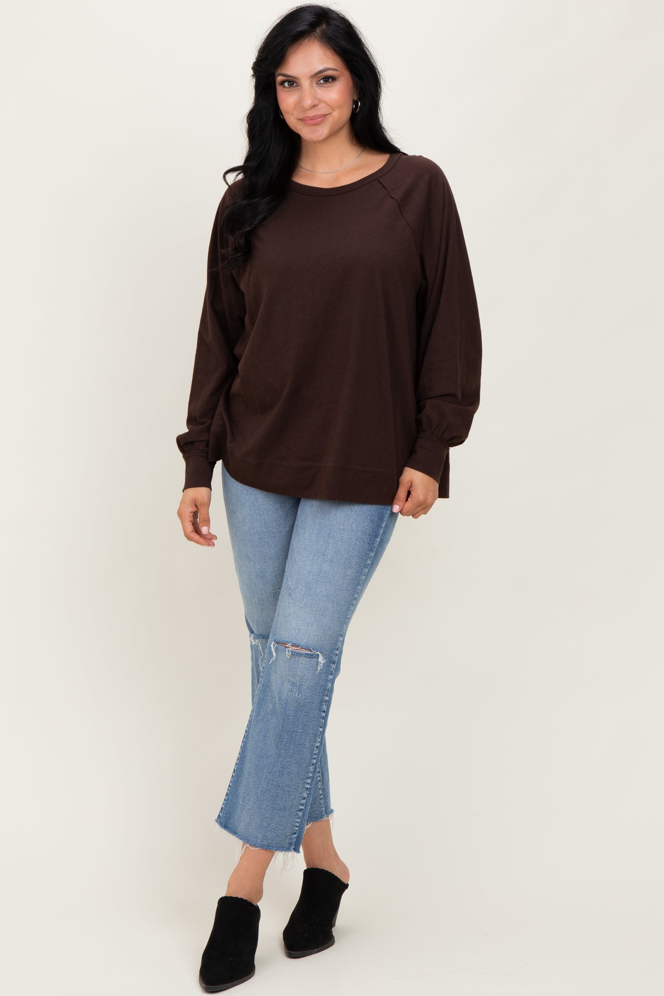 woman wearing a brown long sleeve pullover sweatshirt with relaxed fit and distressed light blue jeans