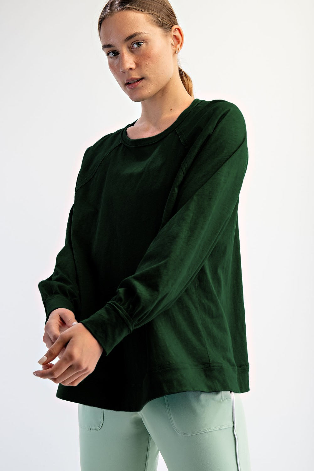 woman wearing a dark green long sleeve top with a relaxed fit and raglan sleeves
