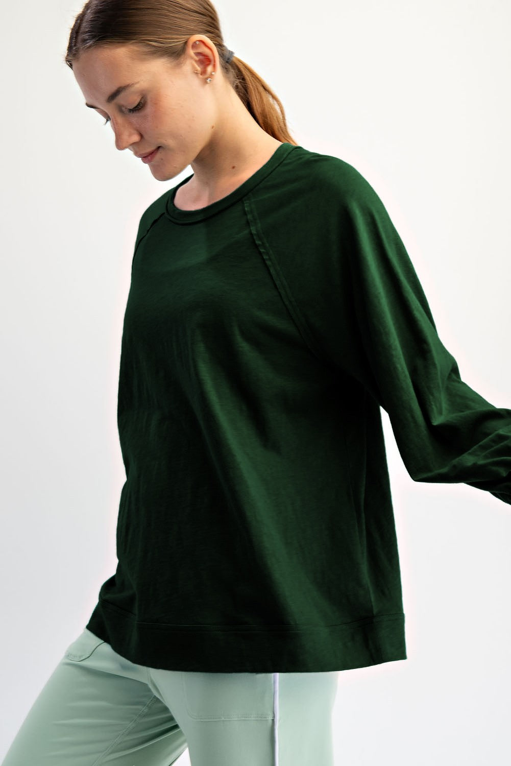 woman wearing a dark green long sleeve pullover sweatshirt with relaxed fit, styled with light green pants