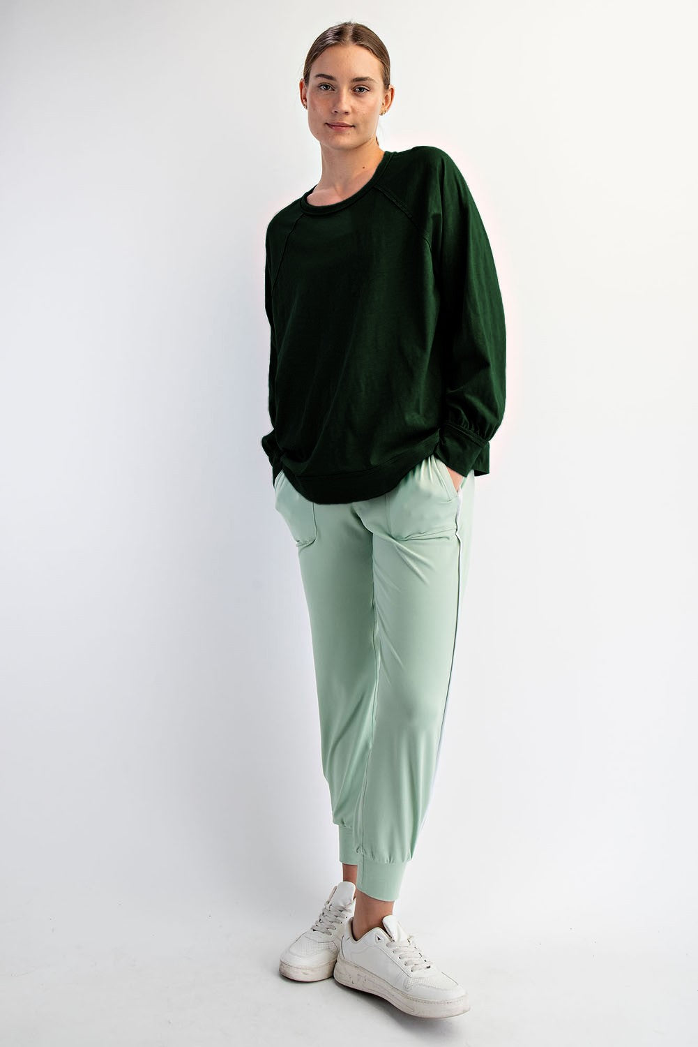 woman wearing a dark green oversized sweatshirt with light green jogger pants and white sneakers