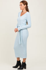 woman wearing a light blue ribbed knit dress with a v-neck and tie belt, standing and facing to the side