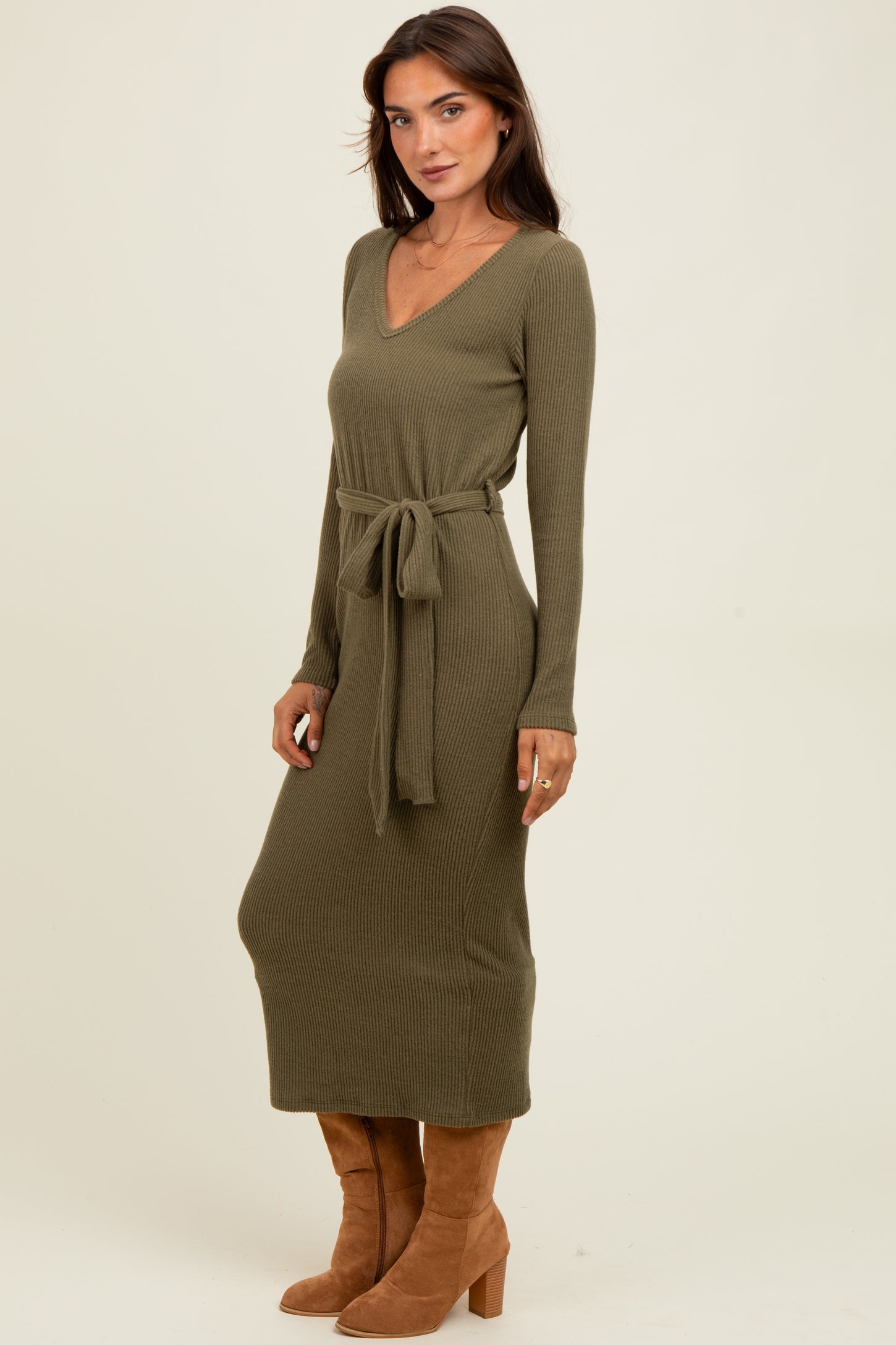 woman wearing a long olive green ribbed knit dress with a tie waist and long sleeves, paired with brown heeled boots
