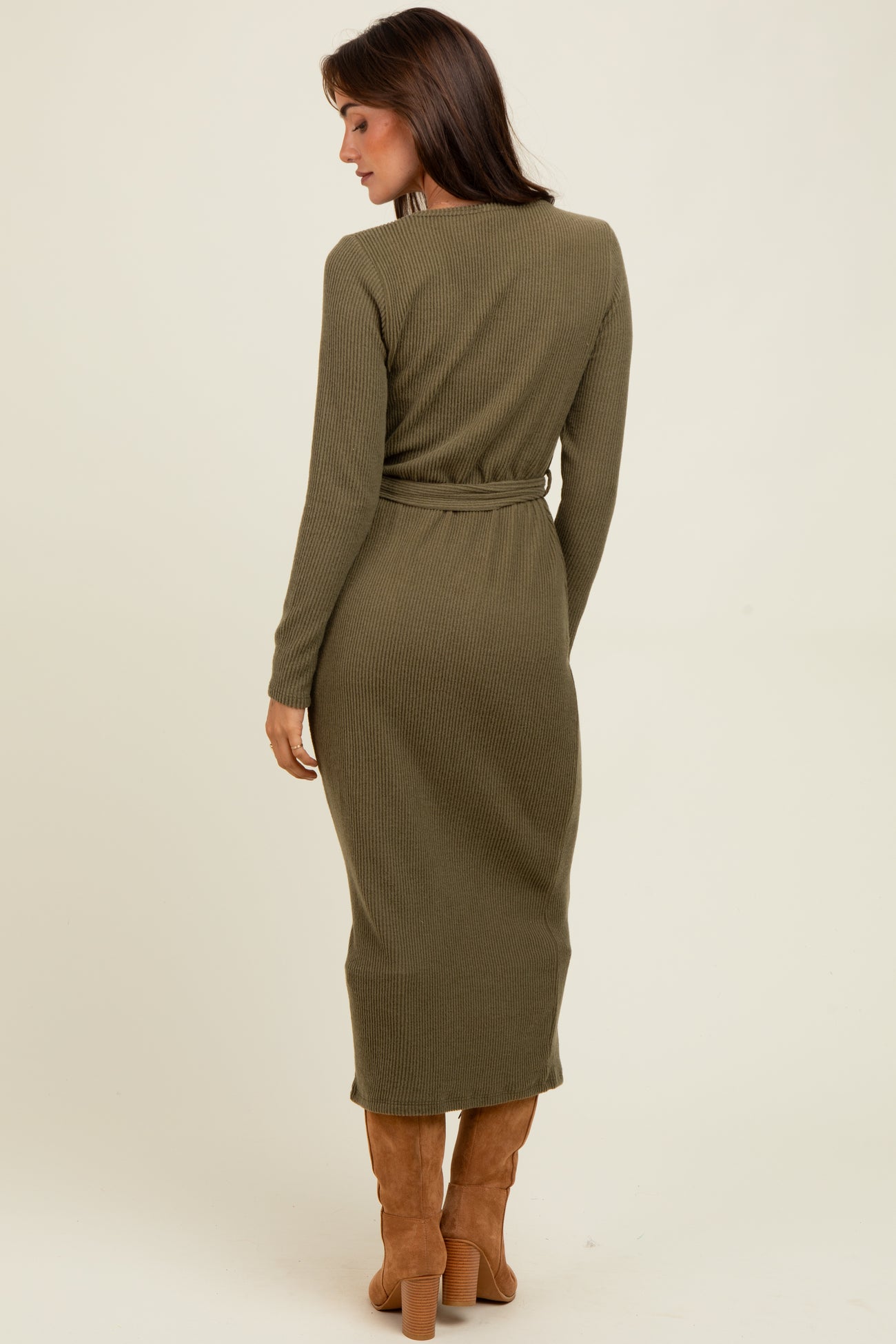 woman wearing a ribbed olive green long sleeve midi dress with a tie waist and thigh-high boots, viewed from the back