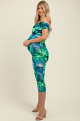 woman wearing a green tropical print off-the-shoulder maternity dress and showing her baby bump