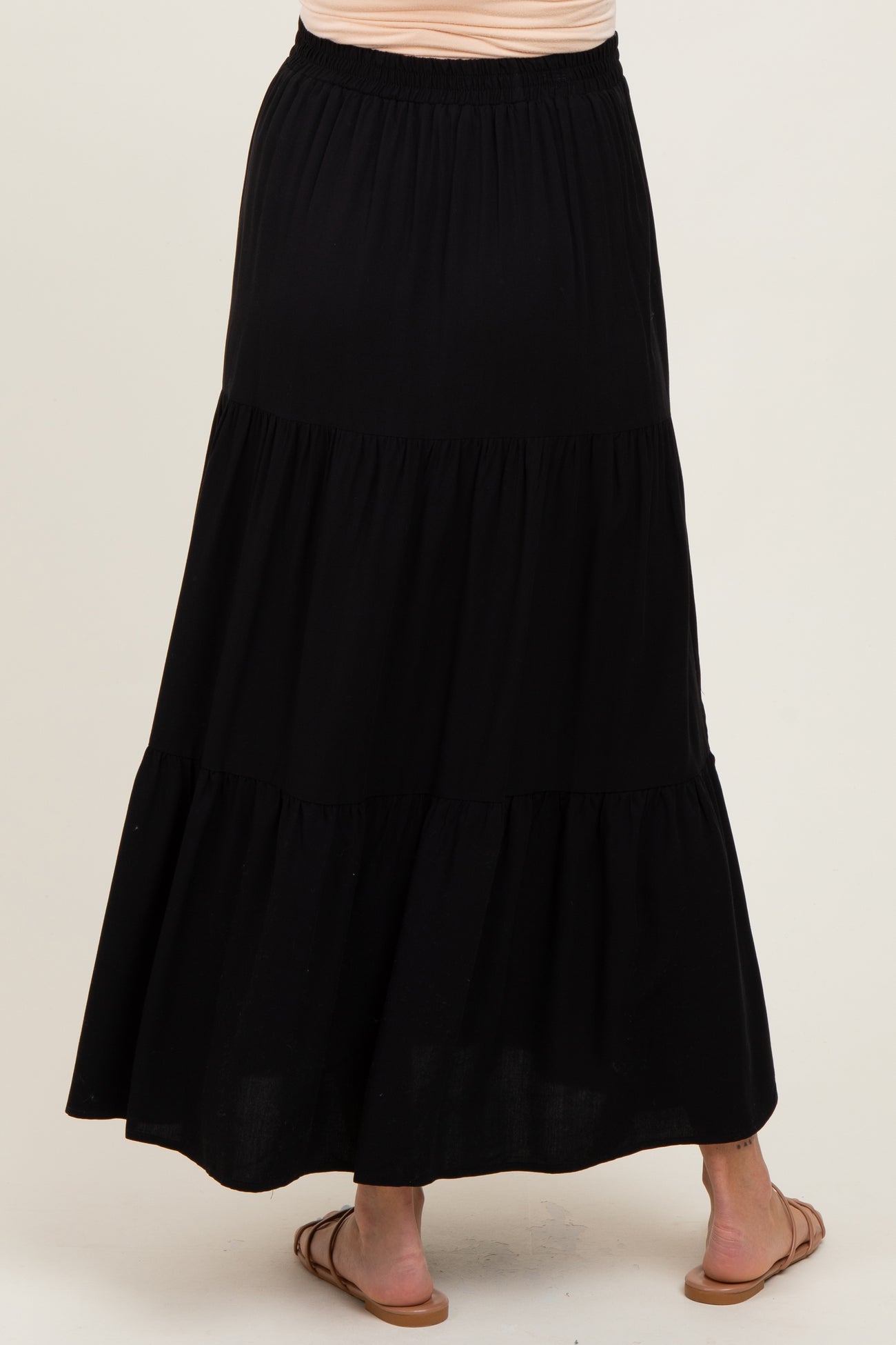 woman wearing a black tiered maxi skirt, showing the back view with a flowy design and elastic waistband, maternity wear