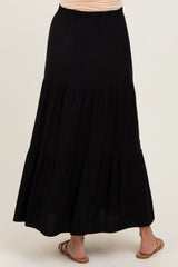 woman wearing a black tiered maxi skirt, showing the back view with a flowy design and elastic waistband, maternity wear