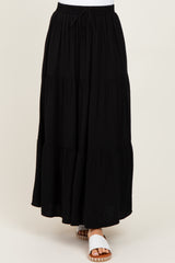 woman wearing a black tiered maxi skirt with an elastic waistband and drawstring detail, paired with white sandals