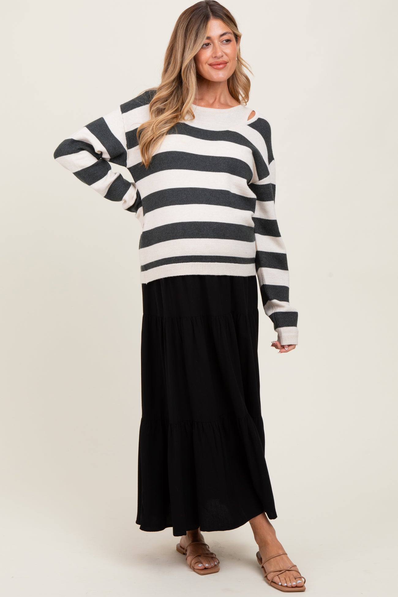 woman wearing a black and white striped maternity sweater with an open shoulder, paired with a black tiered maxi skirt