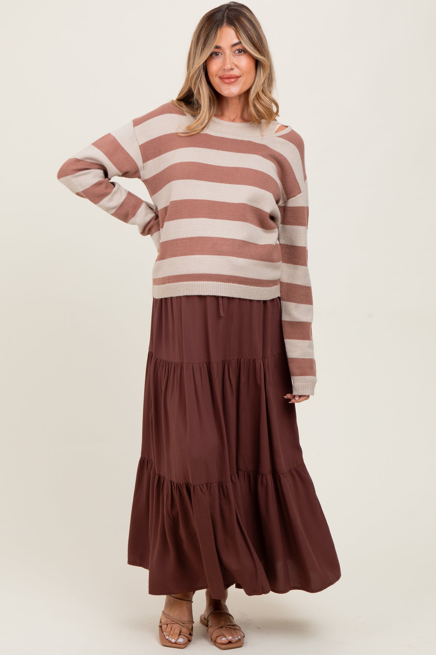 woman wearing a striped brown and beige maternity sweater with a brown tiered maxi skirt and a visible baby bump