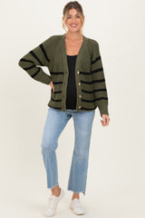 woman wearing a green and black striped maternity cardigan with buttons, paired with light blue jeans and white sneakers, baby bump visible