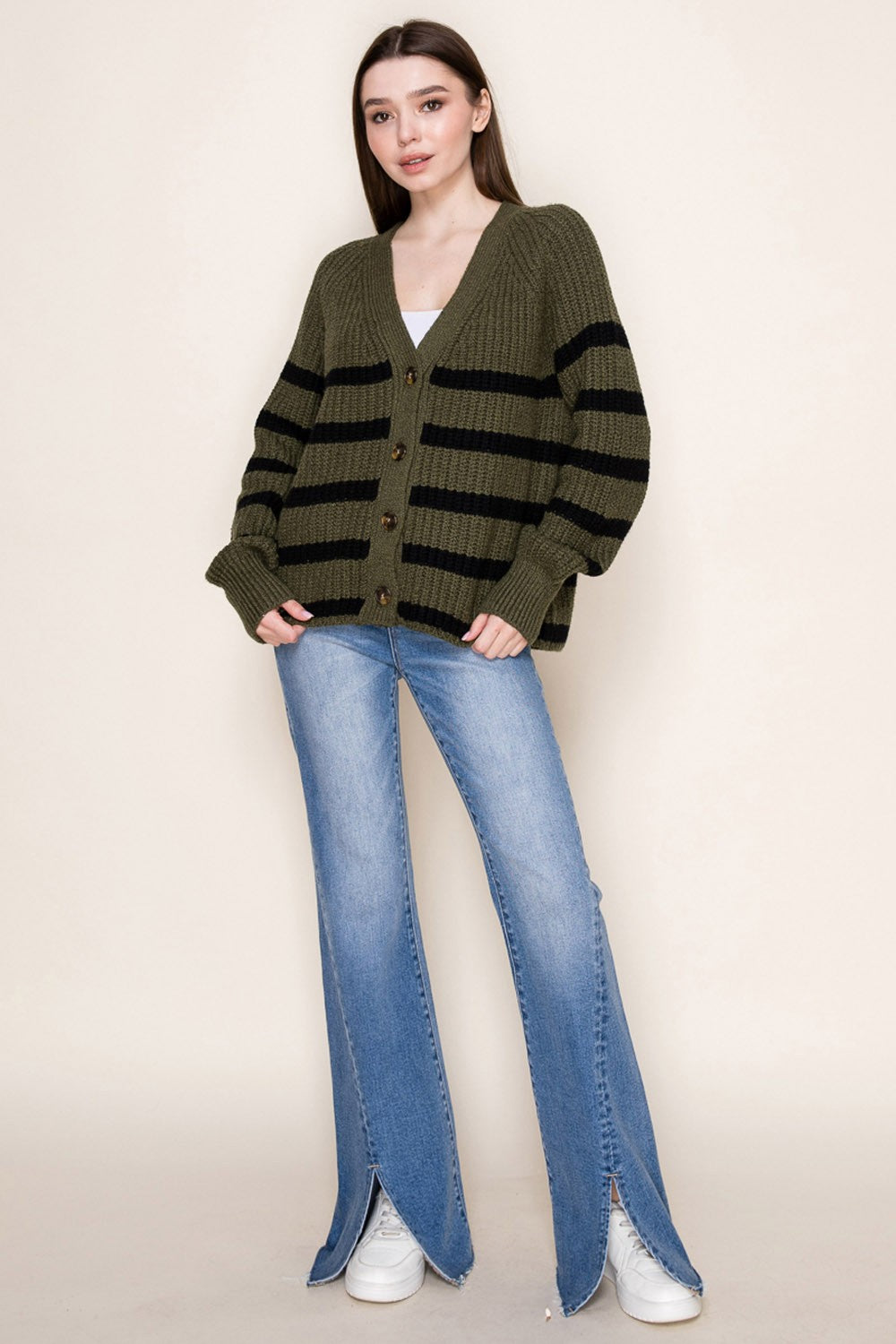 woman wearing an olive green and black striped oversized cardigan paired with light blue split hem flare jeans and white sneakers