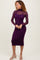 woman wearing a purple long sleeve dress with a sheer overlay and fitted silhouette, standing pose with a smile