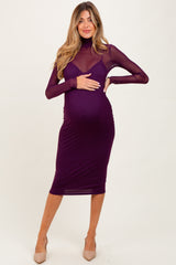 woman wearing a long sleeve purple maternity dress with a fitted silhouette and sheer top, holding her baby bump