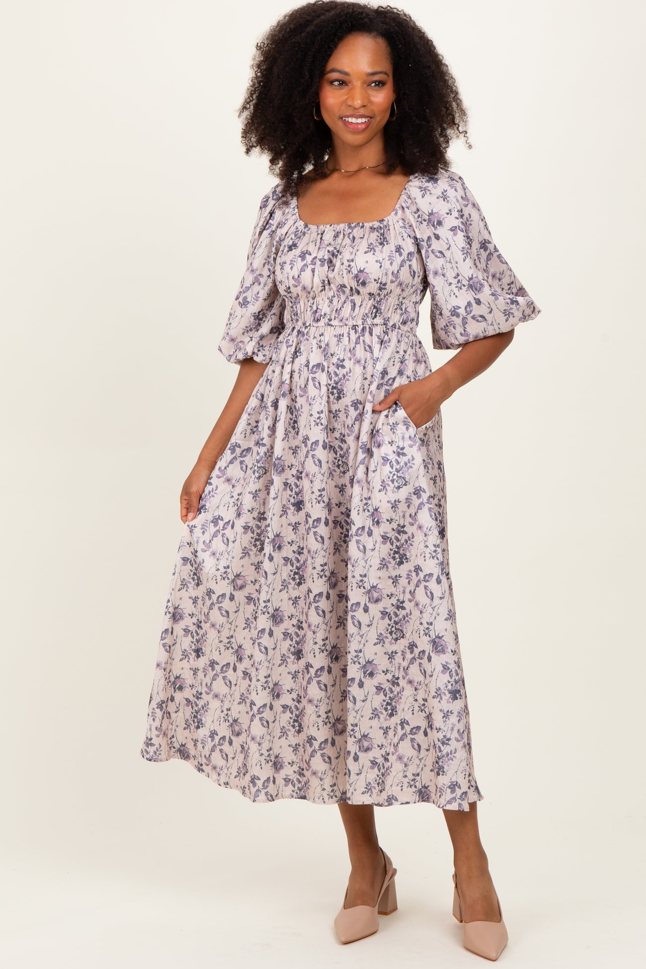 woman wearing a floral print midi dress with puff sleeves and pockets, standing in a neutral background