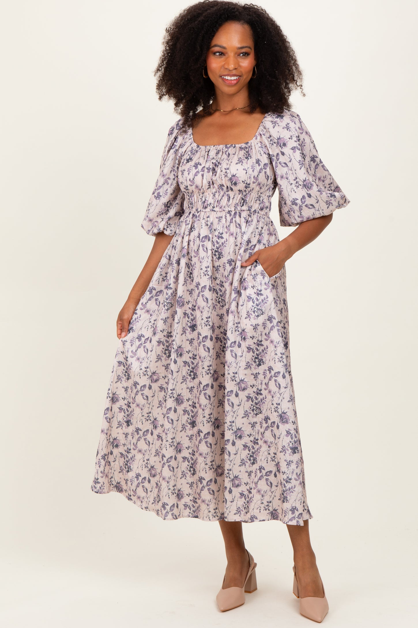woman wearing a floral print midi dress with puff sleeves and pockets, standing in a neutral background