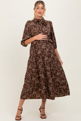 woman wearing a brown floral maternity dress with a tie neck and tiered skirt, holding her baby bump