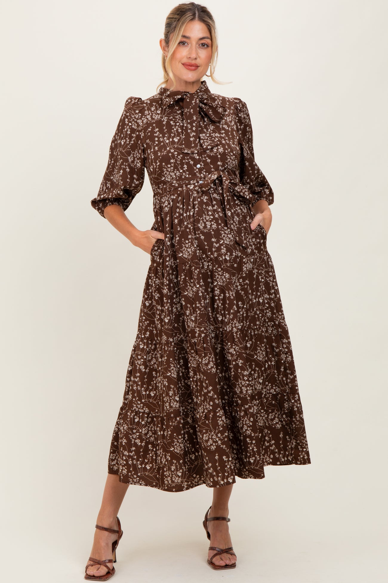 woman wearing a brown floral printed maternity dress with puff sleeves and pockets, styled with heels
