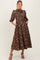 woman wearing a brown floral printed maternity dress with puff sleeves and pockets, styled with heels