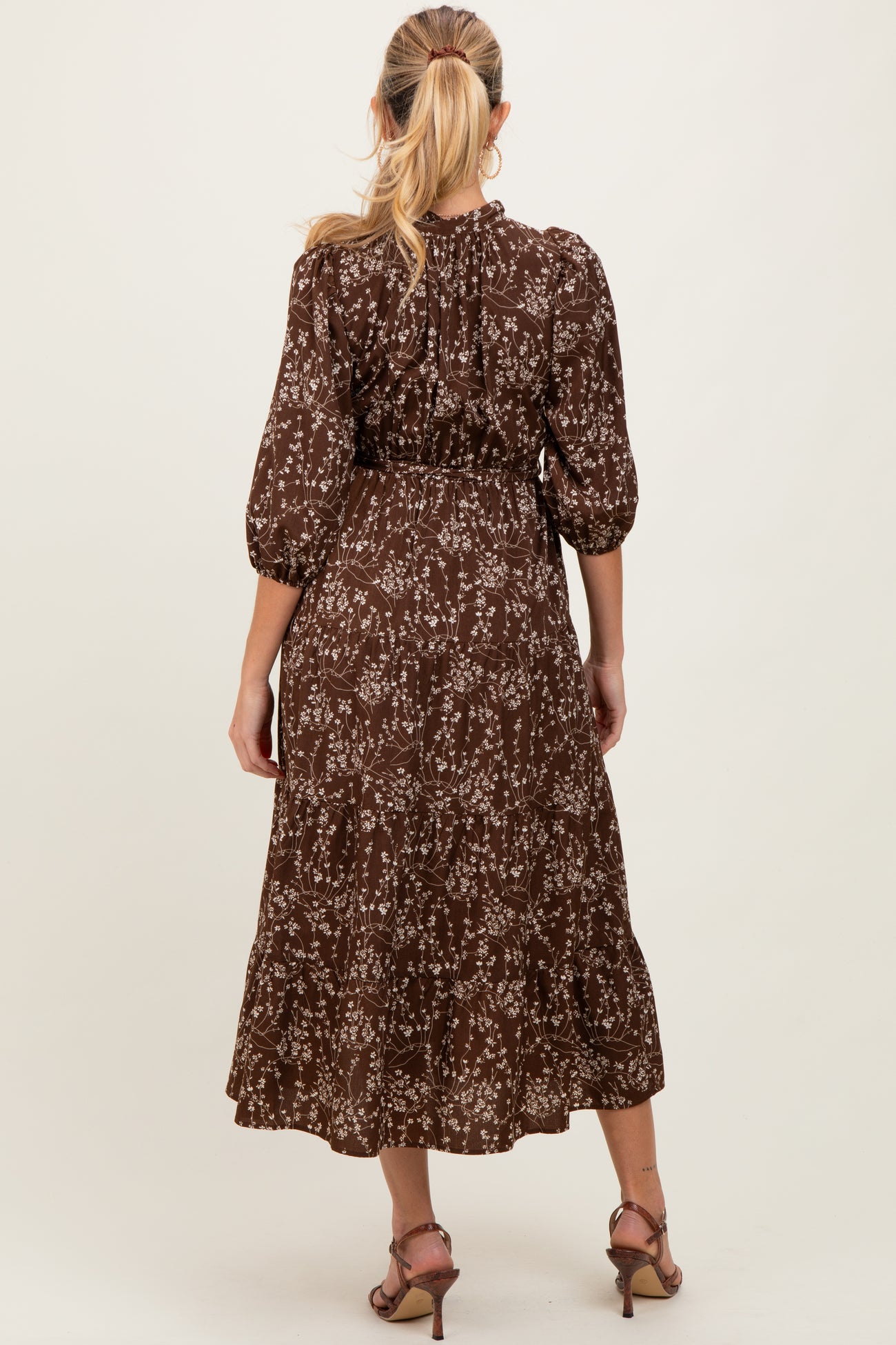 woman wearing a brown floral maternity dress with three-quarter sleeves and a tiered skirt, showing a baby bump