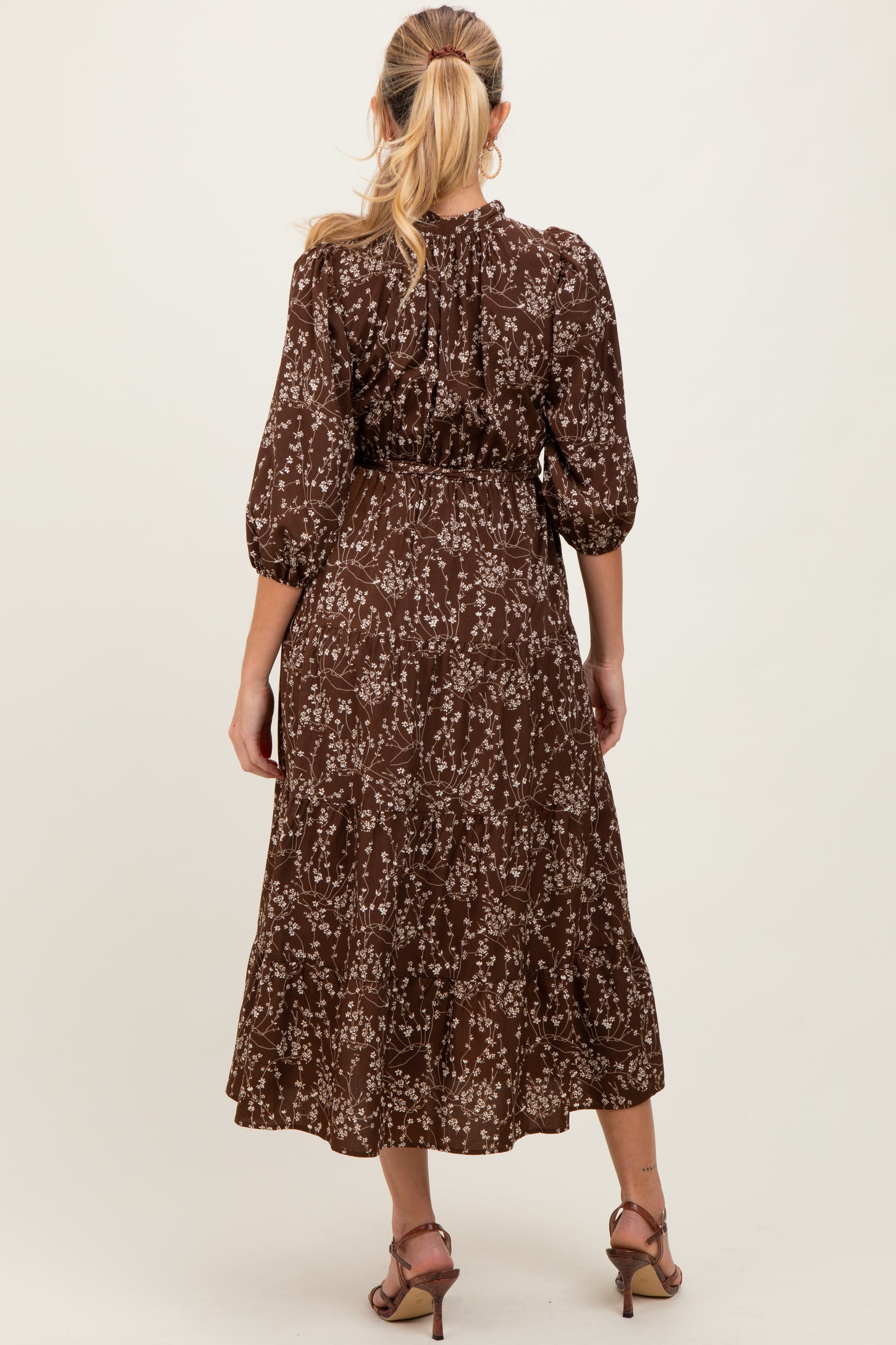 woman wearing a brown floral maternity dress with three-quarter sleeves and a tiered skirt, showing a baby bump
