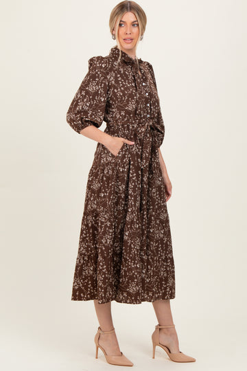 woman wearing a brown floral midi dress with a collar, long sleeves, and pockets, styled with nude heels