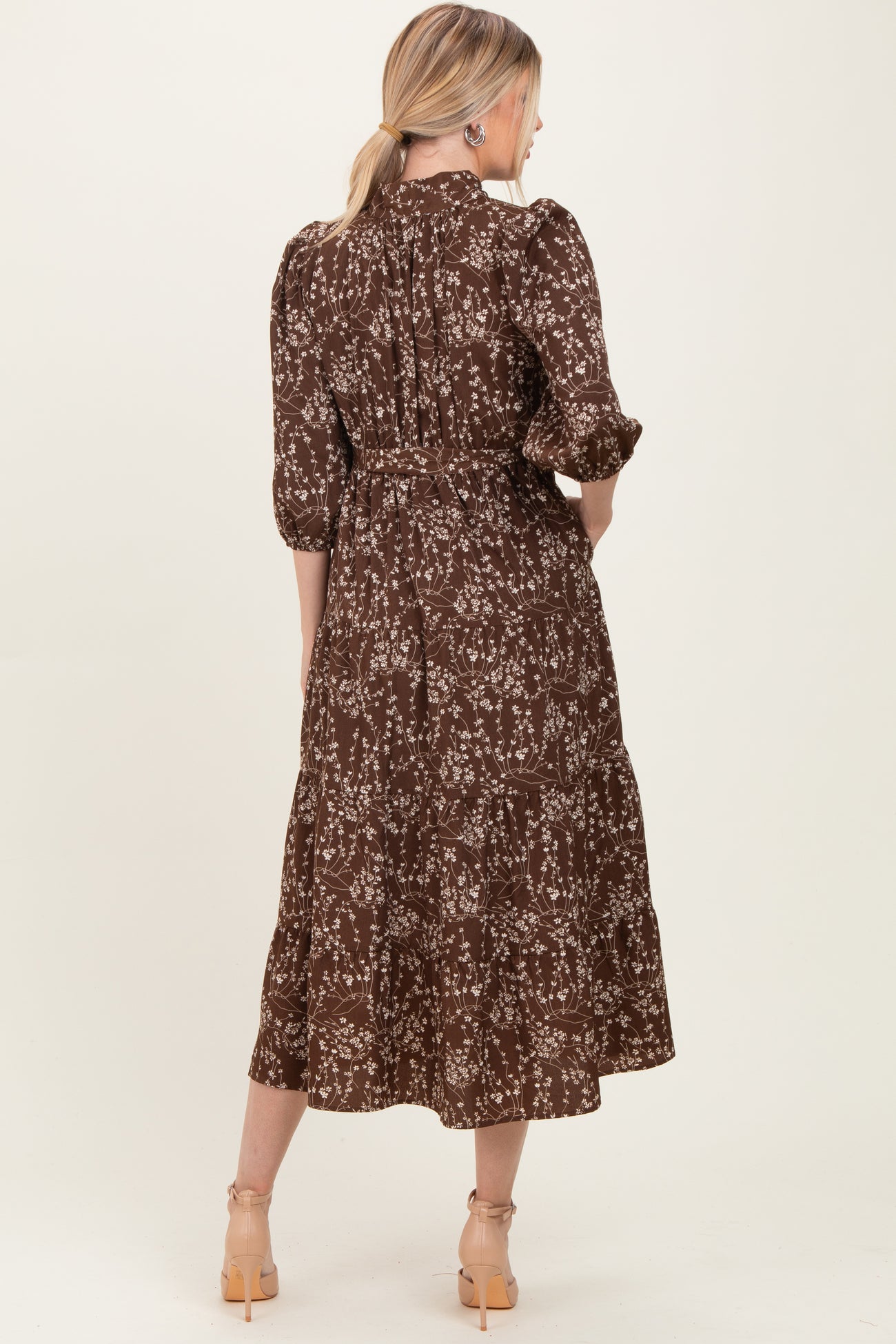 woman wearing a brown floral midi dress with puff sleeves and a tiered design, viewed from the back