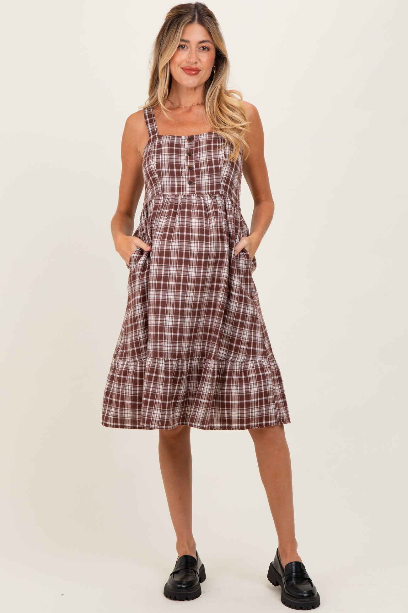 woman wearing a brown and white plaid maternity dress with pockets and a tiered skirt