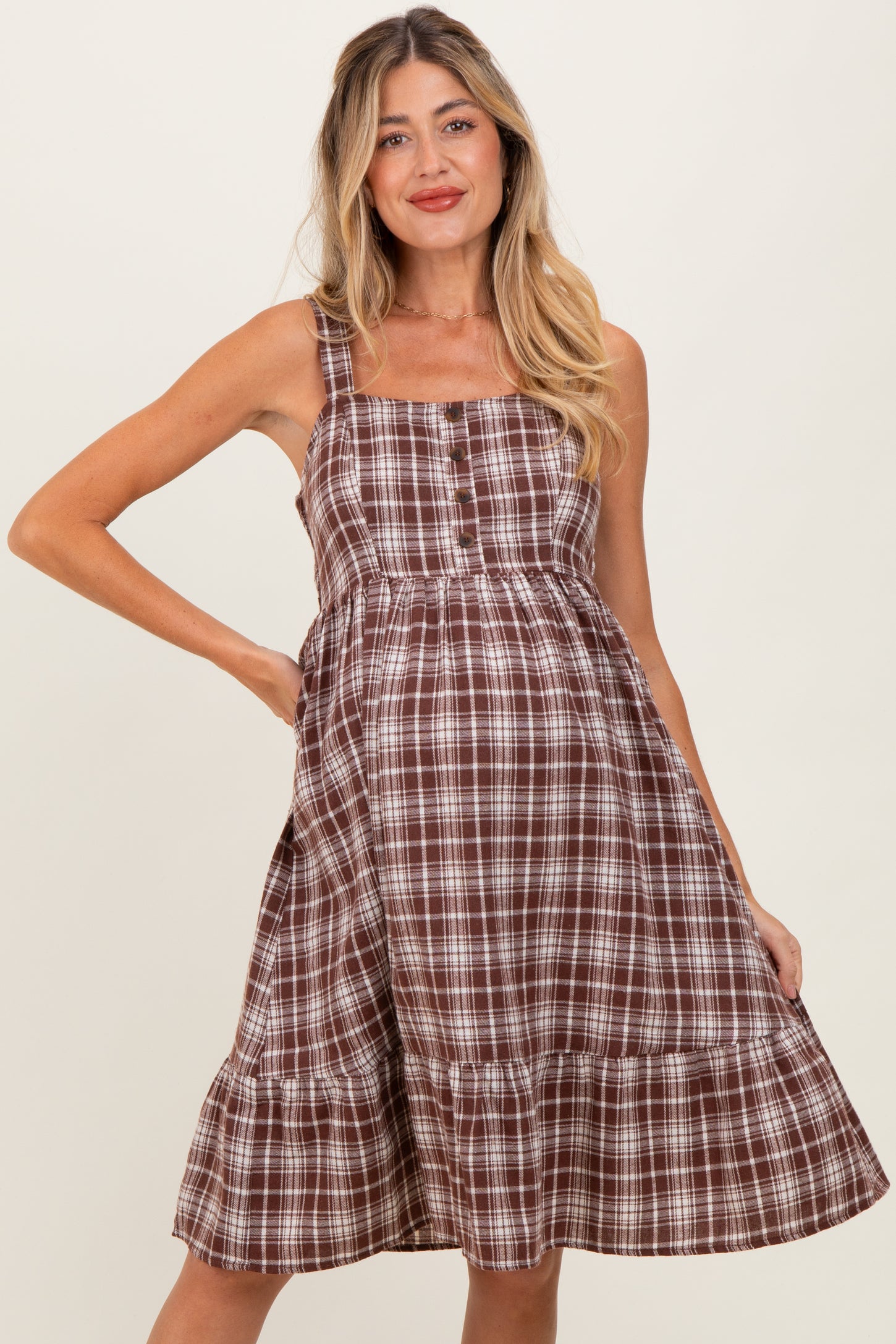 woman wearing a brown and white checkered maternity dress with spaghetti straps and a tiered hemline