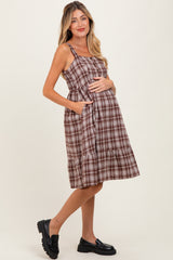 woman wearing a brown plaid maternity dress with pockets and a ruffled hem, showing her baby bump