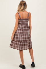woman wearing a brown plaid maternity dress with adjustable straps and a tiered skirt, showing her baby bump from behind