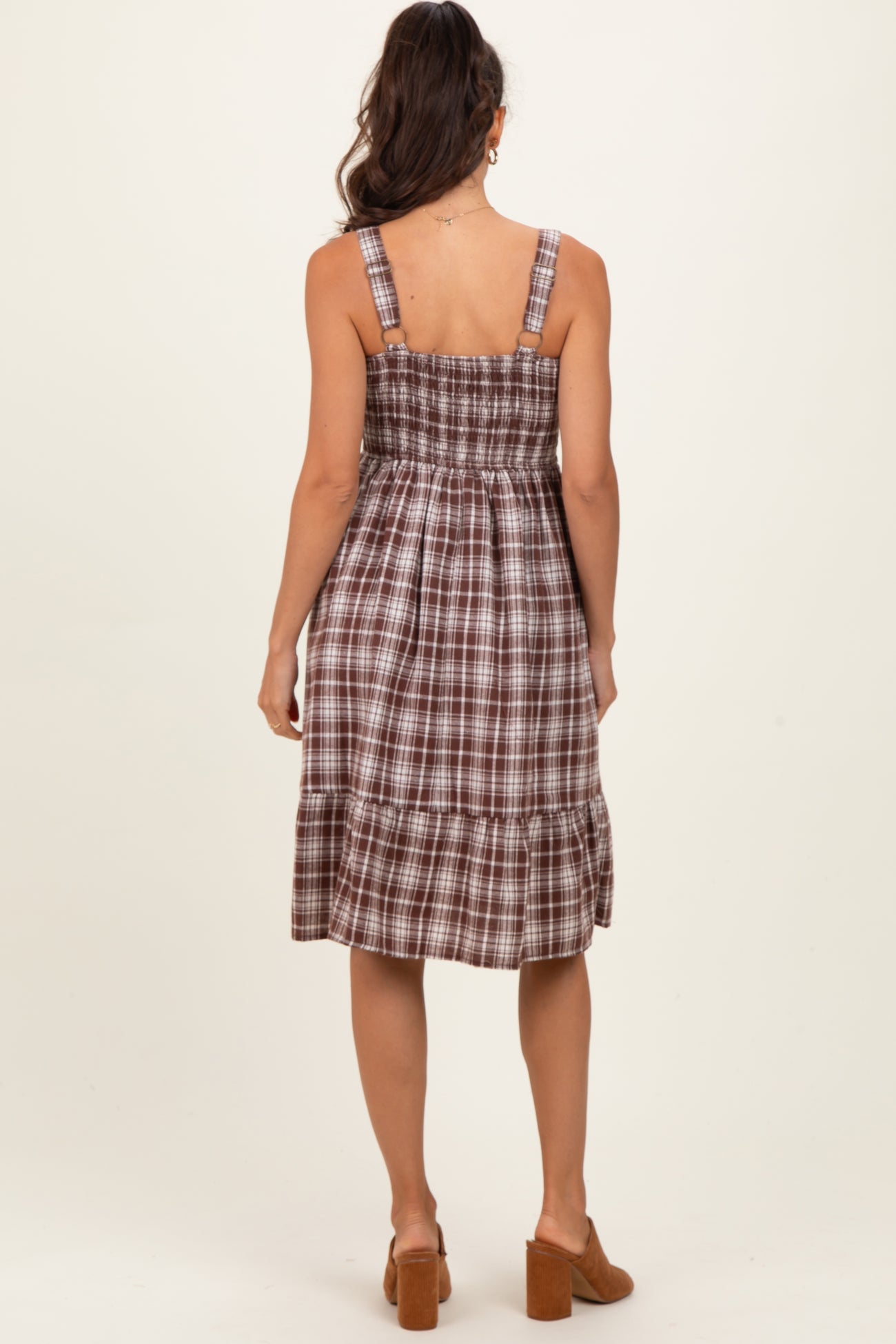 woman wearing a brown plaid smock dress with adjustable straps and a tiered skirt, viewed from the back