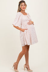 woman wearing a pink floral maternity dress with puff sleeves and pockets, holding her baby bump
