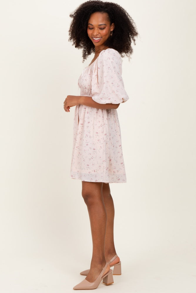 woman wearing a light pink floral print short sleeve dress with a fitted waist and flowy skirt, standing sideways