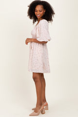 woman wearing a light pink floral print short sleeve dress with a fitted waist and flowy skirt, standing sideways
