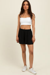 woman wearing a white cropped tank top and black athletic shorts, standing against a plain background