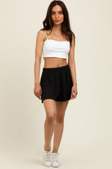 woman wearing a white fitted crop top and black pleated shorts with a casual stance