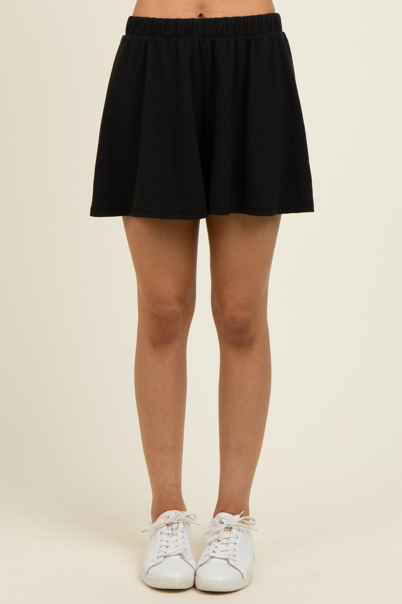 woman wearing a black pleated skater skirt with an elastic waistband and white sneakers