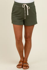 woman wearing green ribbed maternity shorts with a drawstring waist and pockets, standing against a neutral background