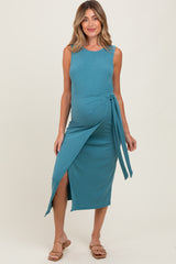 woman wearing a teal sleeveless maternity dress with a tie waist and thigh slit, showcasing her baby bump