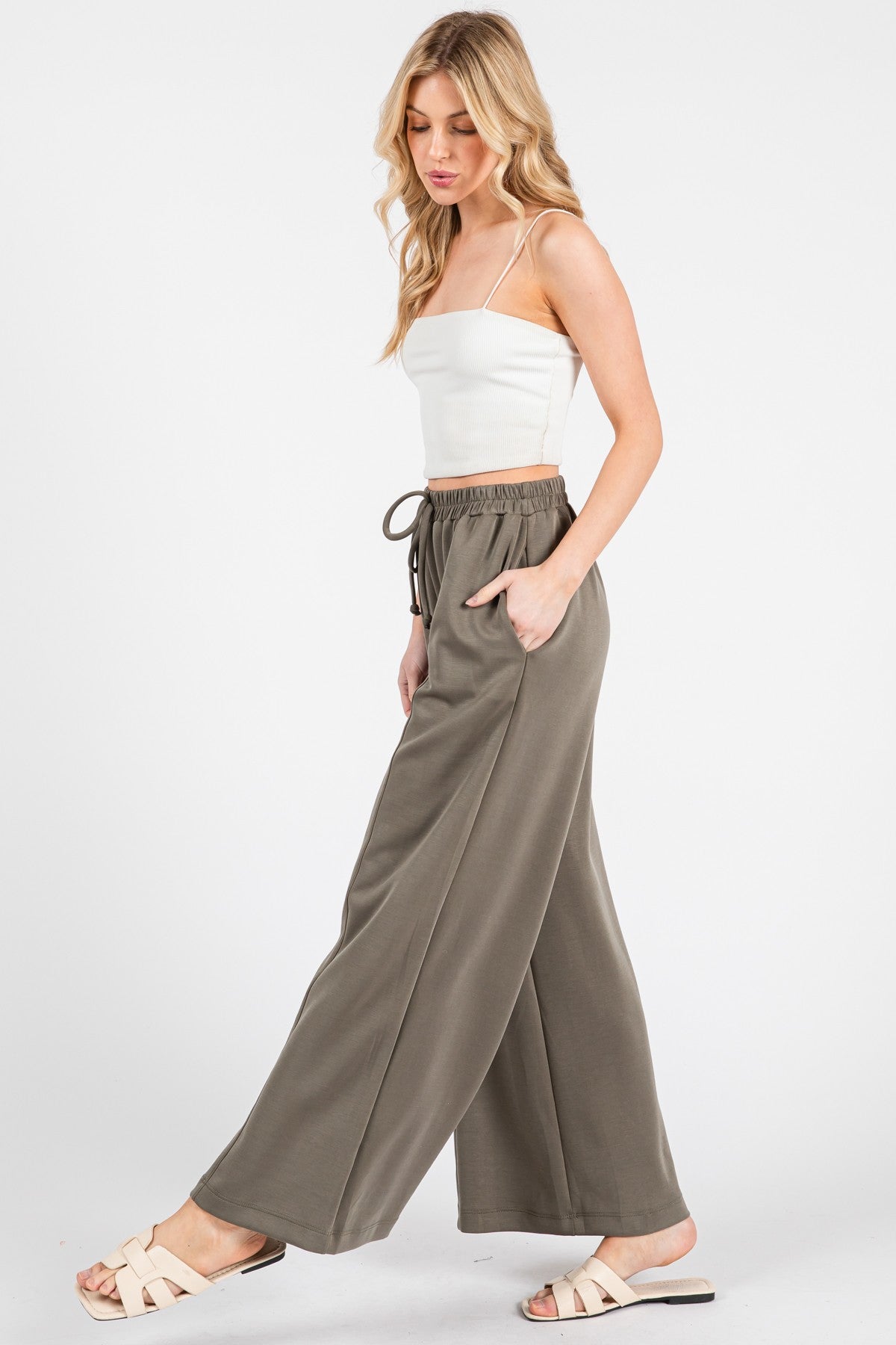 woman wearing a white cropped tank top and olive green wide-leg pants with pockets and a drawstring waistband