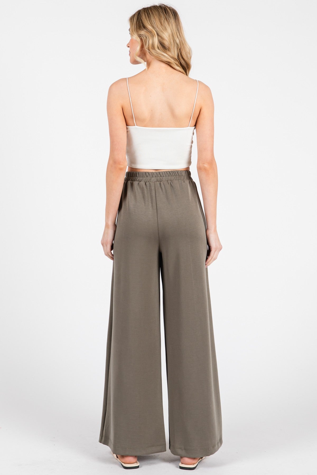 woman wearing a fitted white crop top and high-waisted wide-leg olive green pants, shown from the back