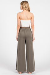 woman wearing a fitted white crop top and high-waisted wide-leg olive green pants, shown from the back