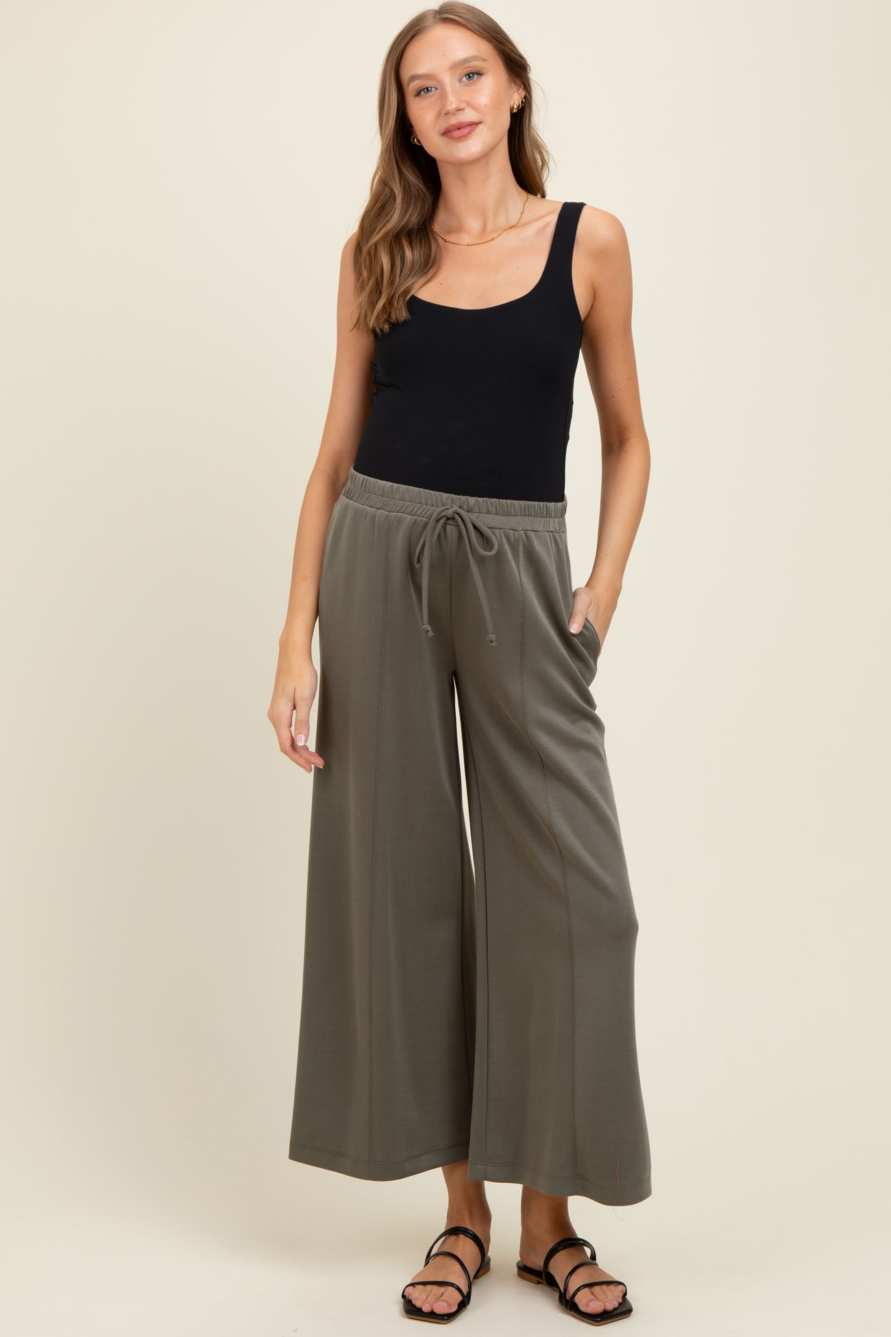 woman wearing a black tank top and olive green wide-leg maternity pants with pockets