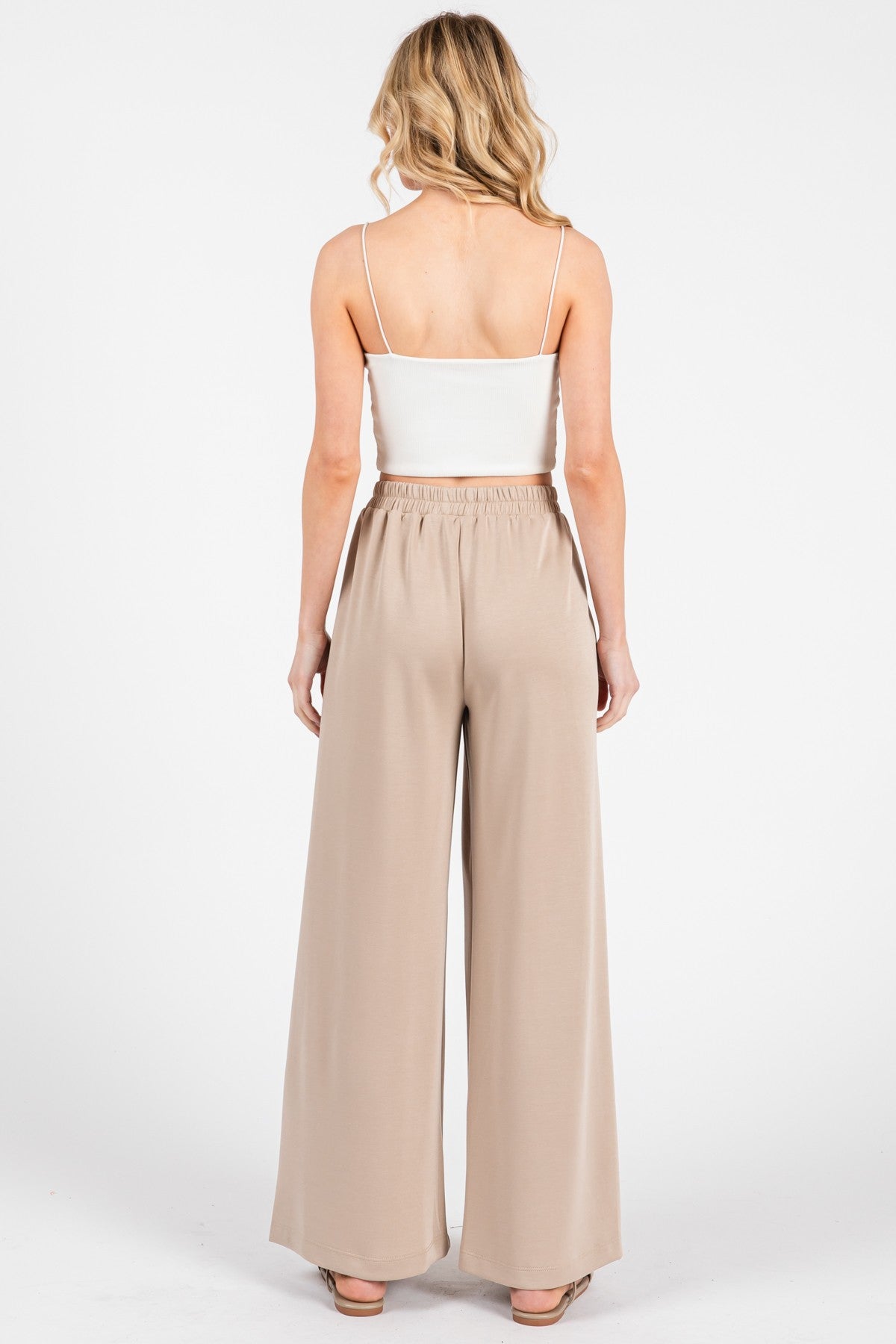 woman wearing a white spaghetti strap top and beige wide leg trousers, showing the back view of the outfit