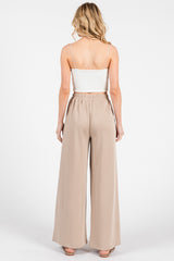 woman wearing a white spaghetti strap top and beige wide leg trousers, showing the back view of the outfit